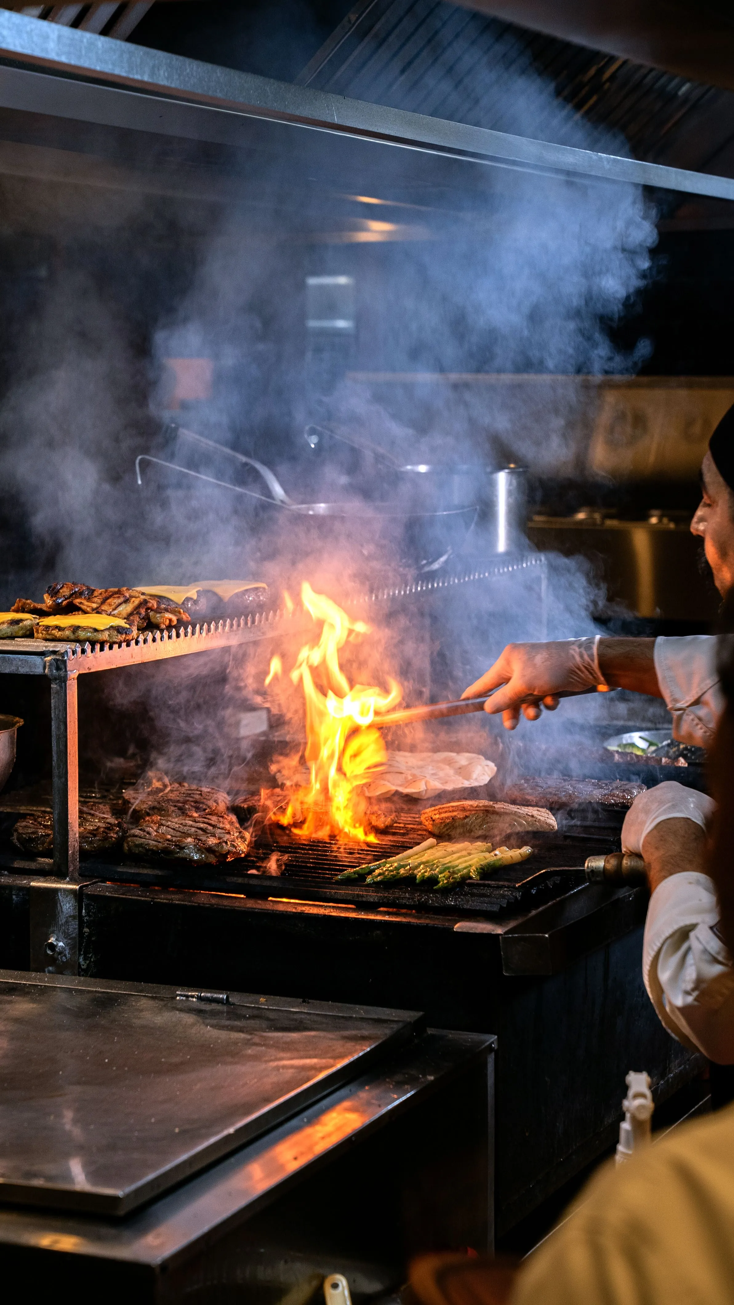Parrillero avivando el fuego de la brasa en la cocina de Asador Artebe, con humo y llama