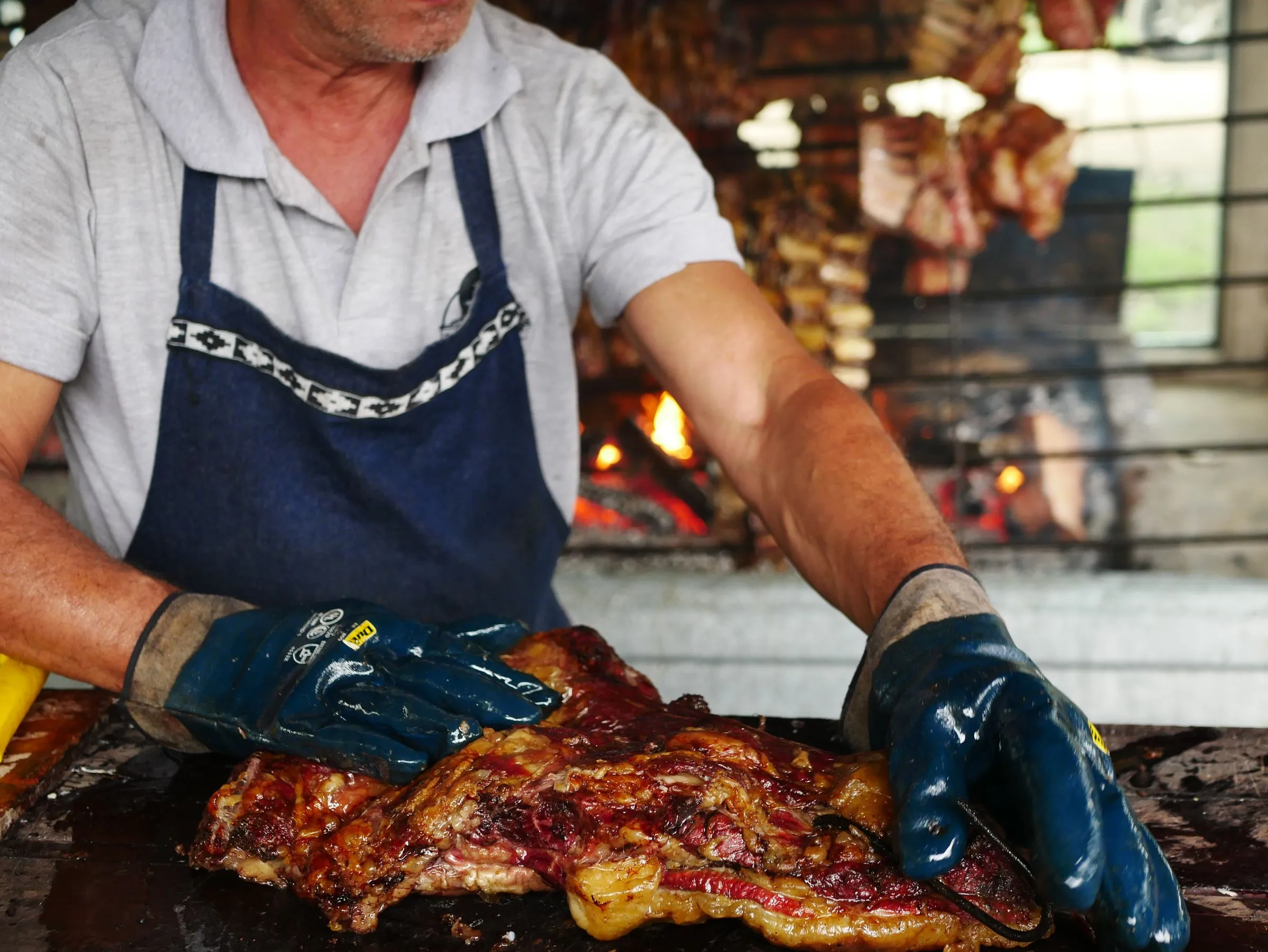 Manos del parrillero preparando una pieza de carne junto a las brasas